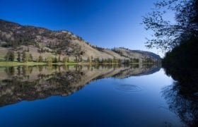 Looking out across a still lake mirroring the hill in the background in the water.